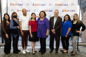 An image of eight individuals posing in front of a backdrop of the Talk On Alzheimer's step and repeat
