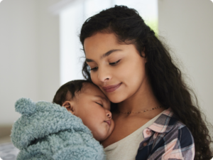 A person holding a baby wrapped in a blue blanket, with the baby sleeping peacefully on their shoulder.
