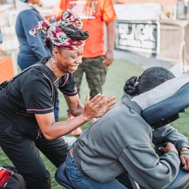 Photo of a woman giving a back massage to a person sitting face down in a massage chair