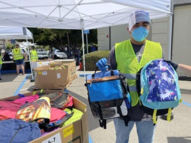 Photo of a volunteer holding up two school backpacks at an event for donating school supplies