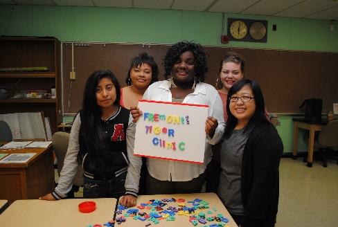 Picture of 5 women standing in a classroom facing the camera with the middle woman holding a sign