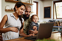 Photo of a mother, father and toddler in a kitchen looking at a laptop