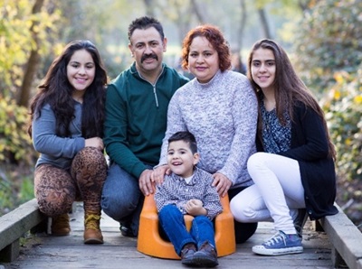 Photo of a family kneeling on a park walkway around a small child sitting in a support chair
