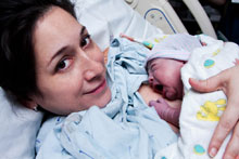 Photo of a new mom in recovery laying in bed holding her newborn baby.