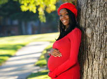 Photo of a pregnant woman leaning against a tree holding her belly.