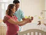 Photo of a pregnant couple setting up a mobile over a crib