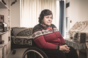 Portrait of the senior disabled Hispanic woman. She is in a wheel chair, wearing casual clothes. Interior of private apartment.