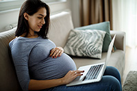 Photo of a pregnant women sitting on a couch working on a laptop