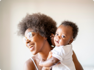 A person wearing glasses holds a baby close, both smiling against a light background.