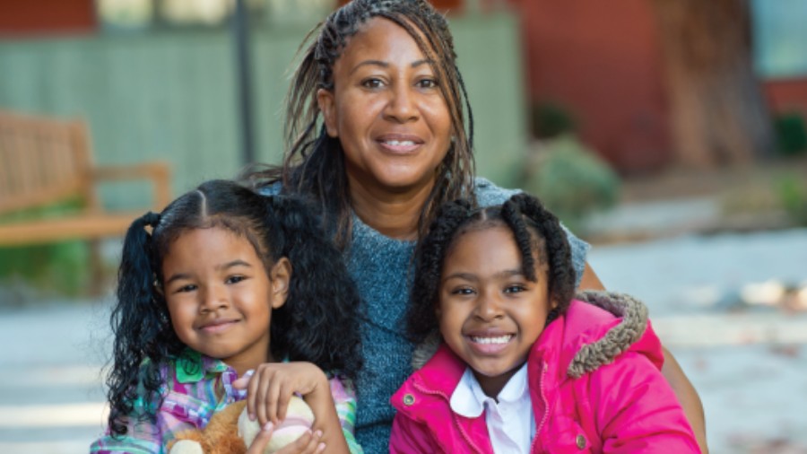 Image of a mother posing and smiling with her two young daughters who sit on her lap.