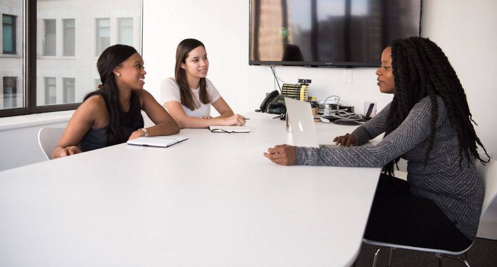 Young professional women at a meeting table, with notebooks and a laptop in front of them. 
