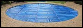 Blue safety cover secured over an in-ground backyard swimming pool surrounded by a concrete deck