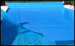 Blue pool cover partially rolled back, revealing clear water in an in-ground swimming pool