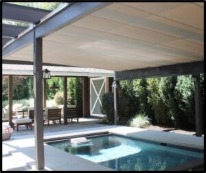 Covered backyard patio with a small rectangular swimming pool, seating area, and surrounding greenery