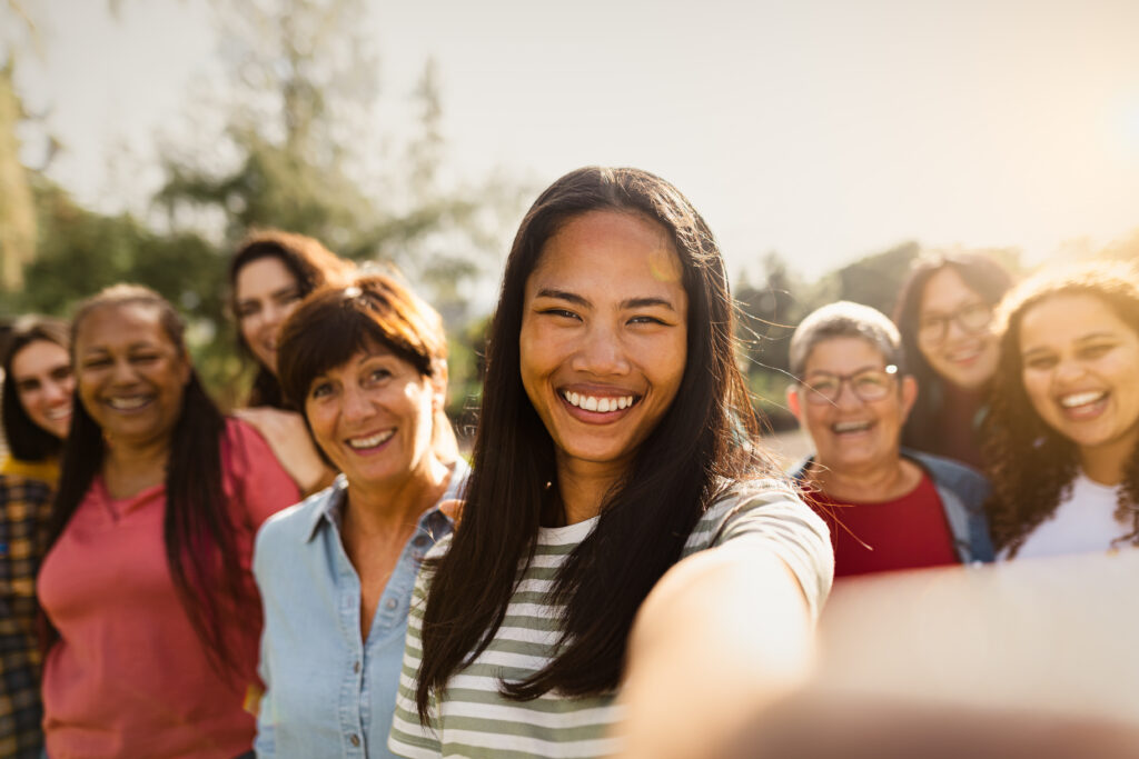 Happy multigenerational group of women with different ethnicities having fun taking selfie with smartphone camera in a public park - Females empowerment concept